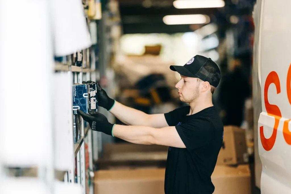 Autotarvikkeen työntekijä keräämässä auton varaosia hyllystä.