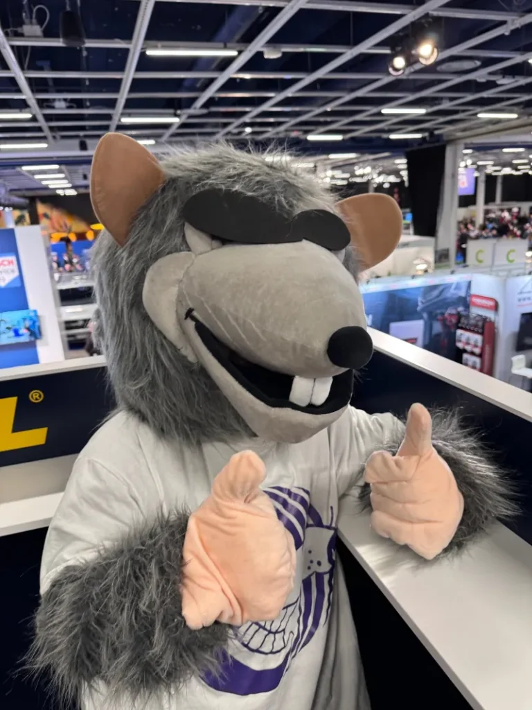 Autotarvikkeen RAT-maskotti peukalot pystyssä automessuilla.