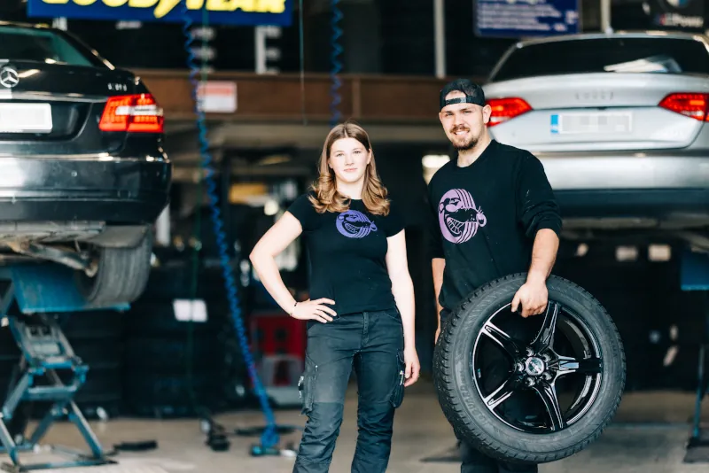 Kaksi Autotarvikkeen työntekijää hallissa, joista toinen pitelee autonrengasta.