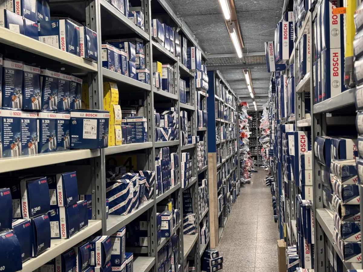 Pitkä varaston käytävä ja hyllyt täynnä varaosia.