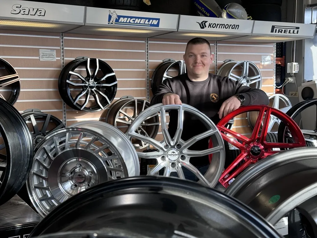 Hymyilevä työntekijä Autotarvikkeen laajan auton vannevalikoiman keskellä.